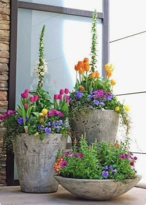 three cement planters filled with colorful flowers sitting on the side of a building next to a window