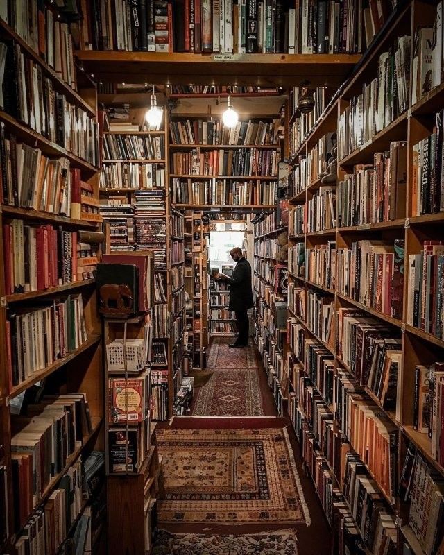 a man is standing in the middle of a library full of books and rugs