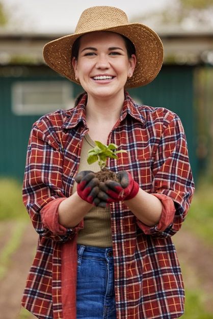 a woman wearing a hat and holding a small plant in her hands while smiling at the camera