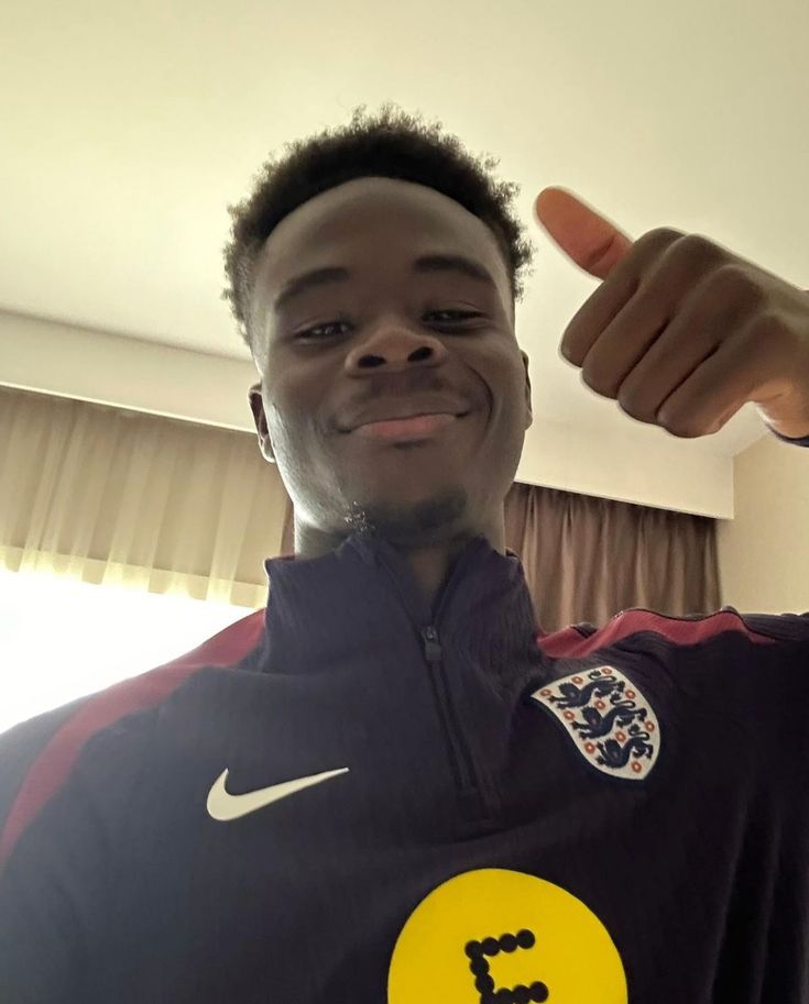 a young man is smiling and pointing to the camera while wearing a shirt with an i love england symbol on it