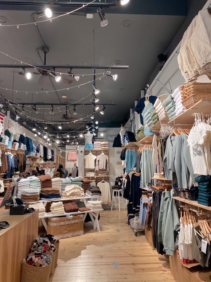 the inside of a clothing store with lots of clothes on racks and hanging lights above