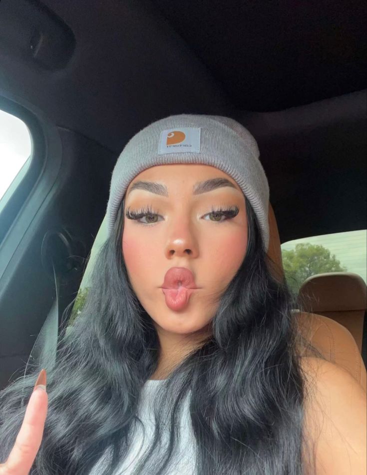 a woman sticking her tongue out in the back seat of a car, wearing a gray beanie