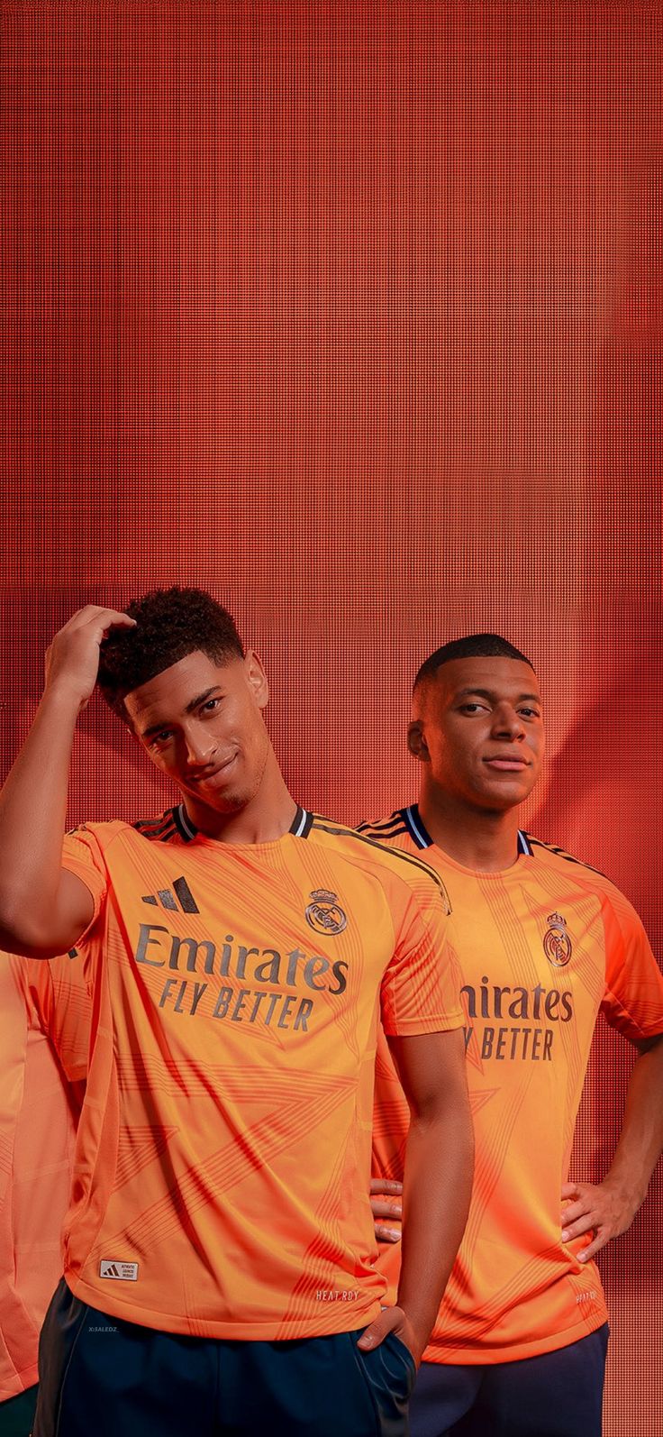 two soccer players pose for a photo in front of a red wall with their hands on their head