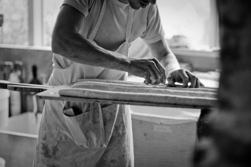 a black and white photo of a man working in a pizza oven with his hands on the board