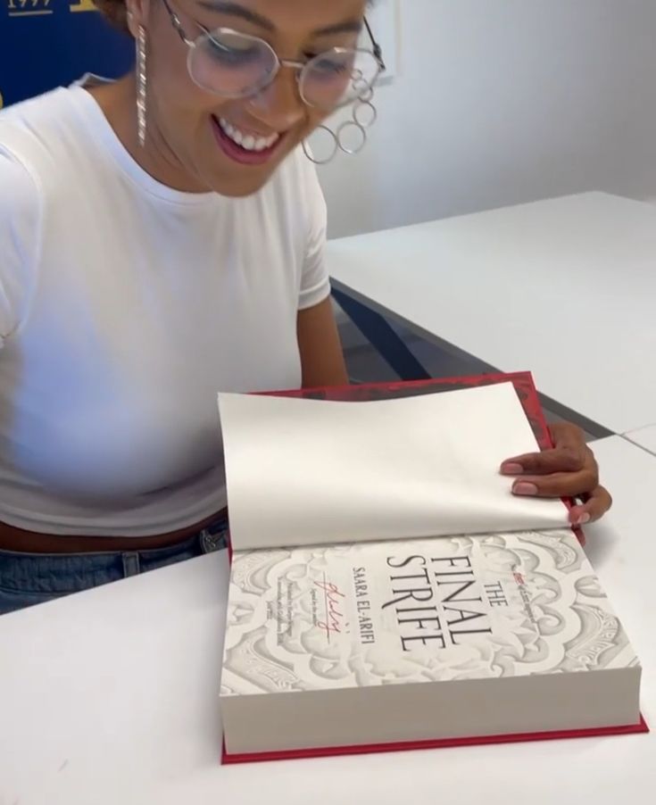 a woman sitting at a table with a book in front of her and reading it