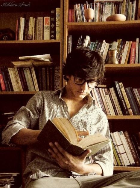 a man sitting in front of a bookshelf reading a book