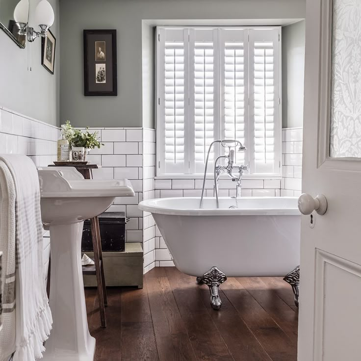 a white bath tub sitting next to a sink in a bathroom with wooden flooring