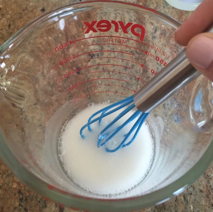 a hand holding a whisk in a glass bowl filled with white and blue liquid