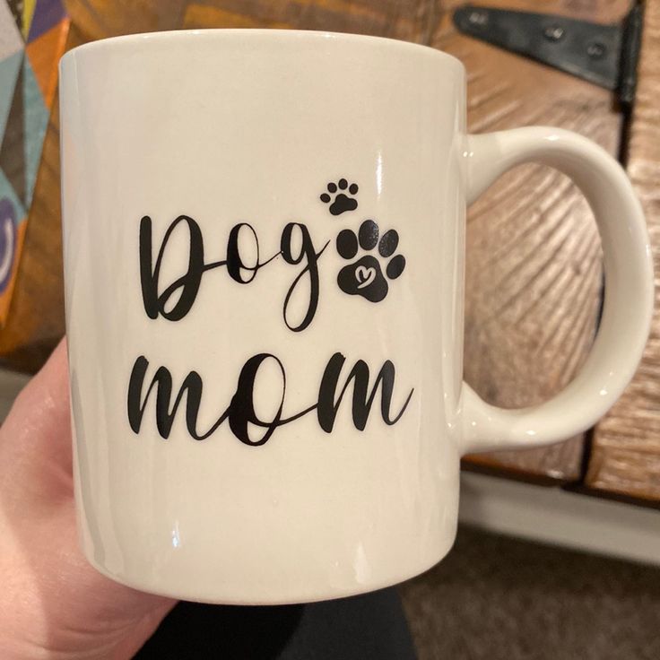 a person holding a coffee mug with the words dog mom written in black on it