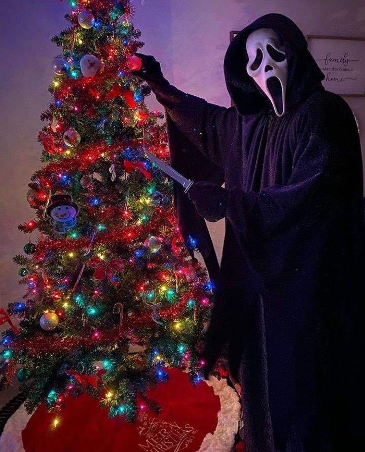 a person in a ghost costume standing next to a christmas tree