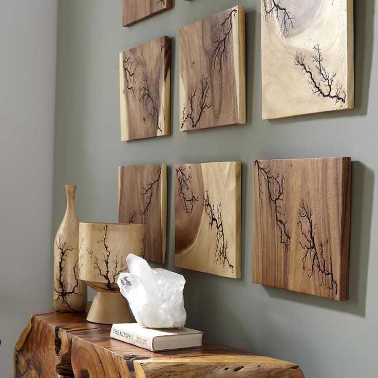 several pieces of art are hanging on the wall above a wooden table with vases