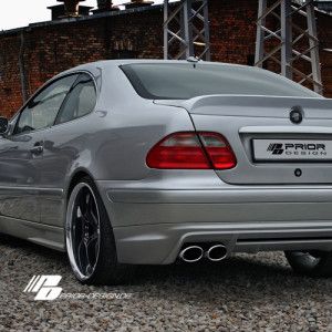 the rear end of a silver car parked in front of a brick wall and building