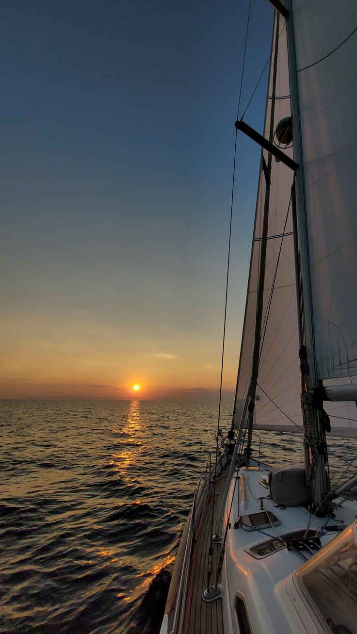 the sun is setting over the ocean on a sailboat