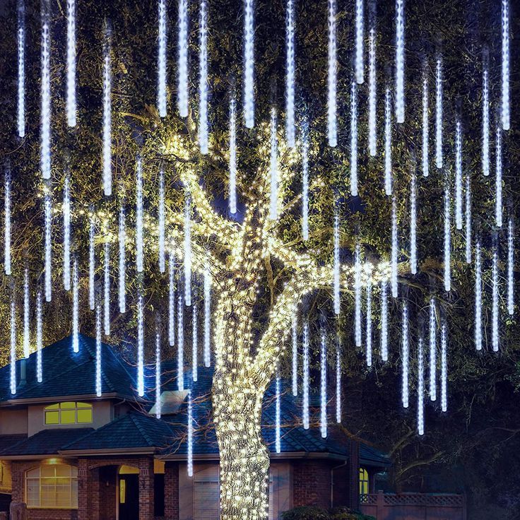 a large tree with lights hanging from it's branches in front of a house