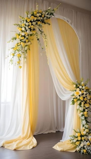 a yellow and white wedding arch with flowers on the front, drapes in the back