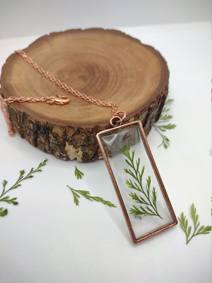 a necklace with a glass pendant hanging from it's side on top of a piece of wood