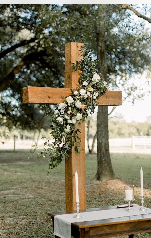 a wooden cross with flowers on it next to a table and candles in the grass