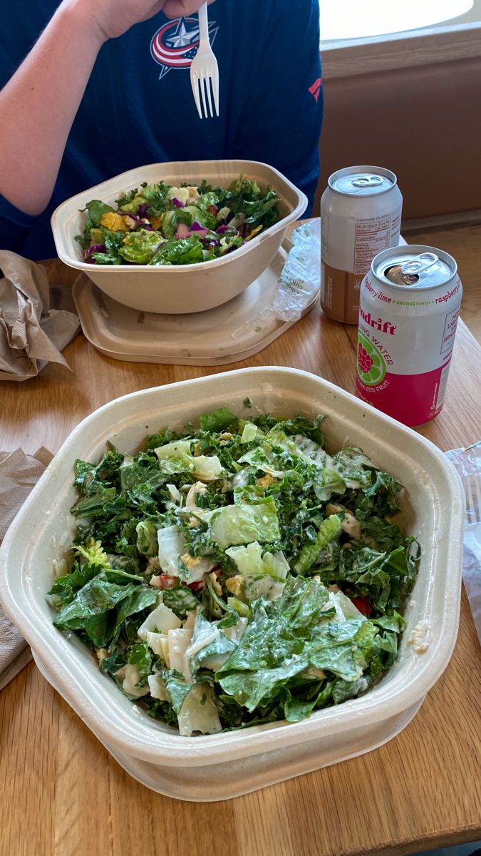 a person sitting at a table with a bowl of salad in front of them and a can of soda