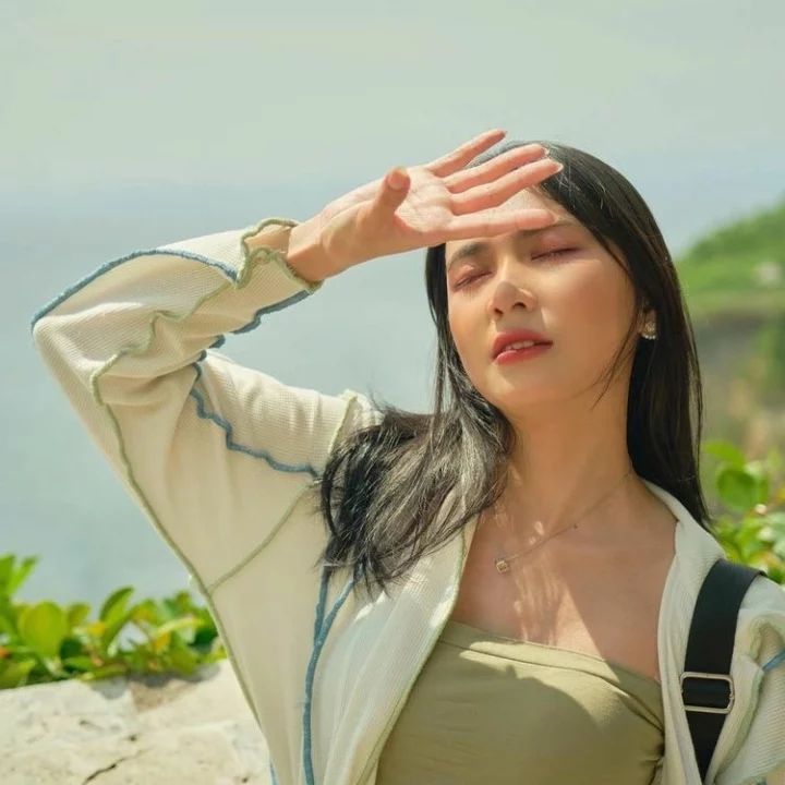 a woman with her hands on her head standing in front of the ocean and holding her eyes closed