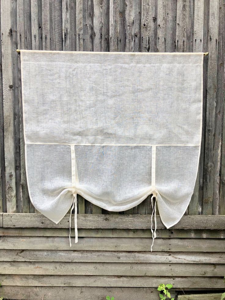 a white curtain hanging on the side of a wooden fence next to plants and flowers