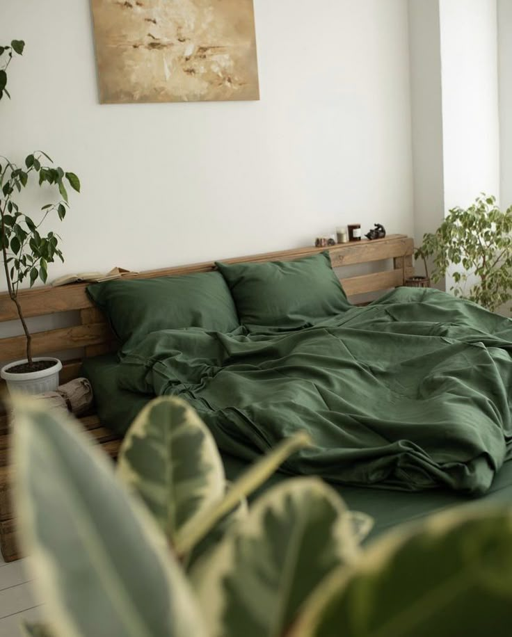 a bed with green sheets and pillows in a room next to a potted plant