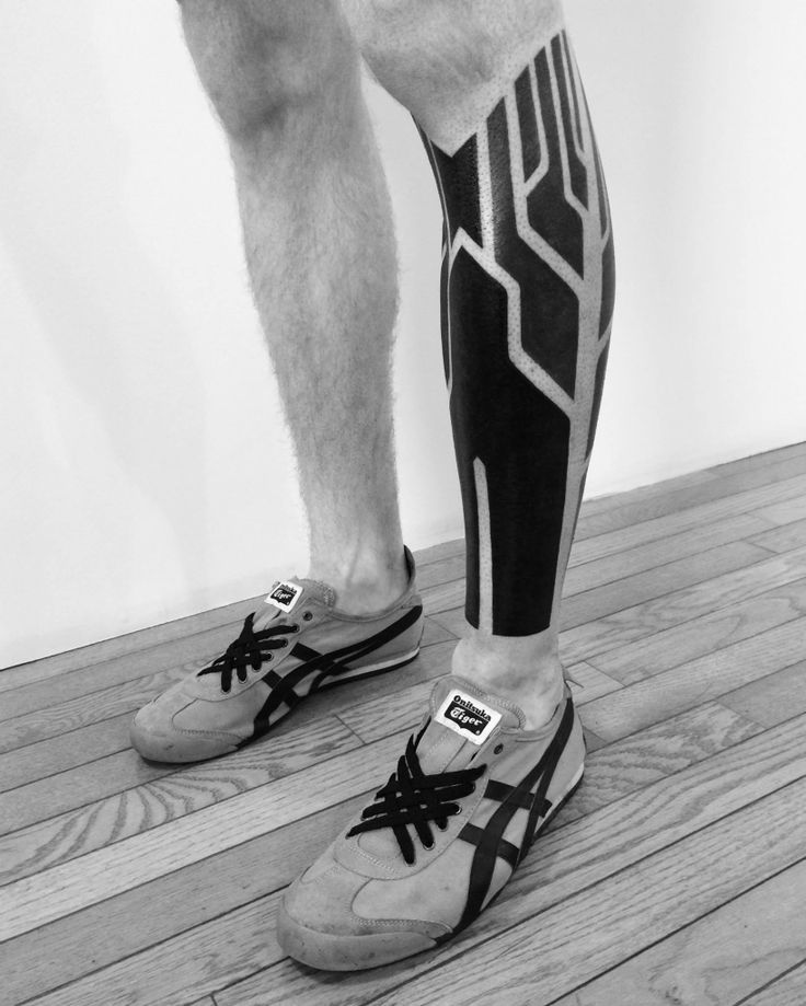 black and white photograph of legs with tattoos on them, standing on wooden floor in front of wall