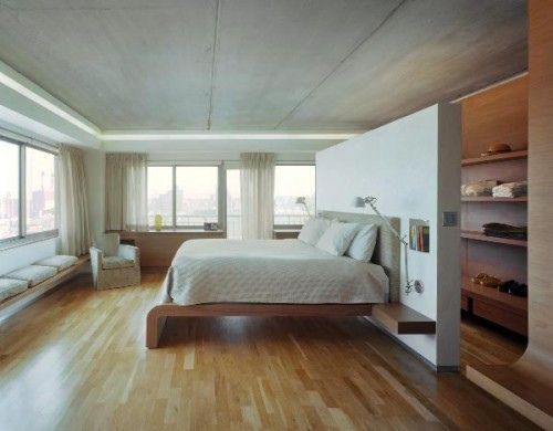 a large bedroom with hardwood floors and white bedding, built in shelving units