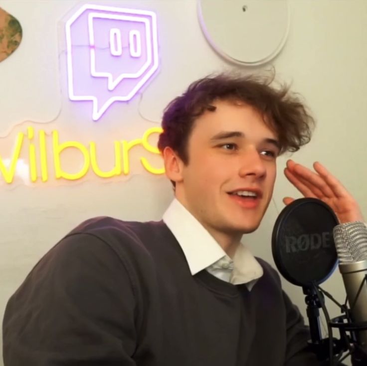 a young man holding a microphone in front of a sign that says vilburs