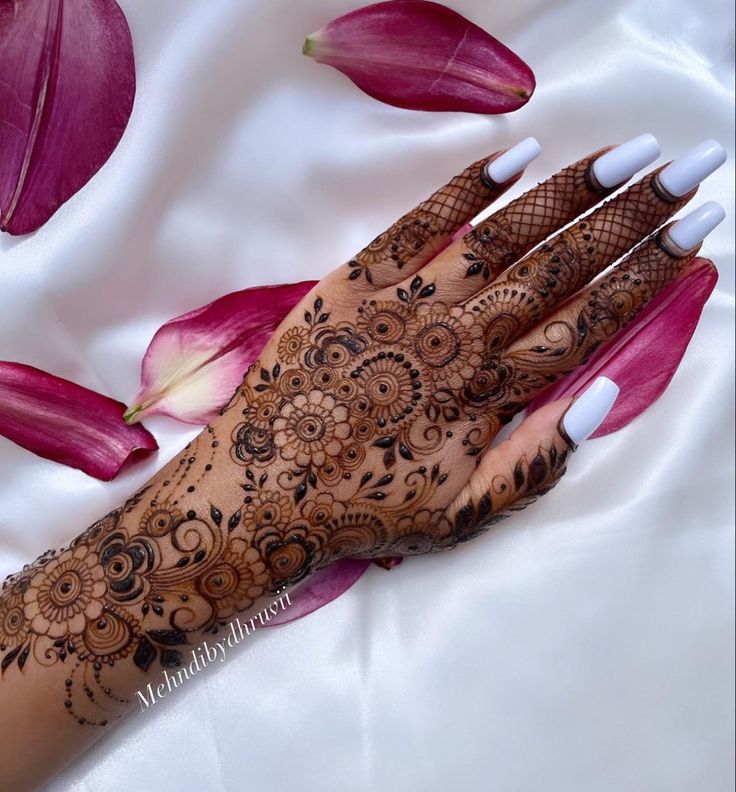 a henna on someone's hand with pink flowers in the background and petals around it