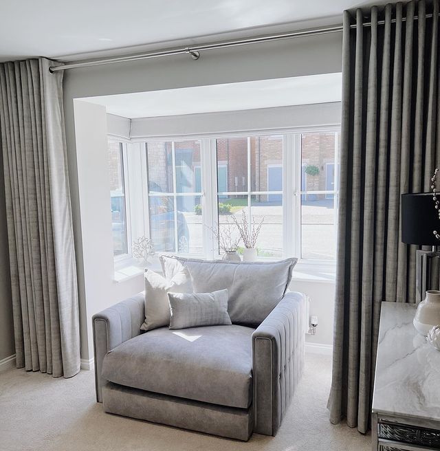 a living room filled with furniture next to a window covered in curtains and drapes