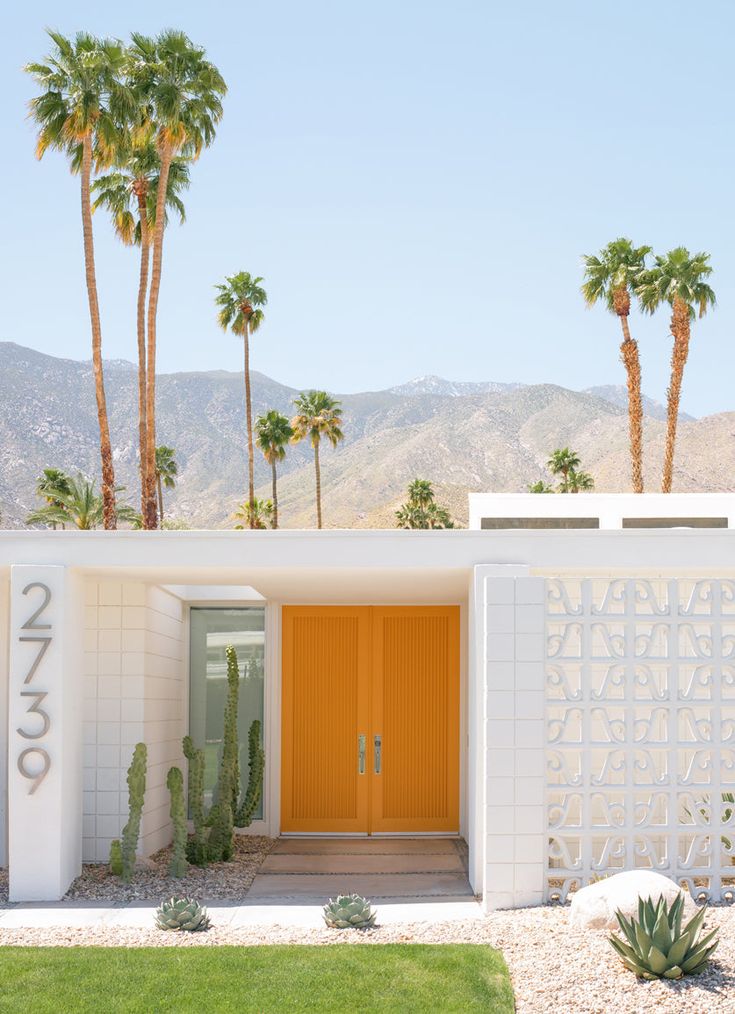 the entrance to a modern home with palm trees and mountains in the background