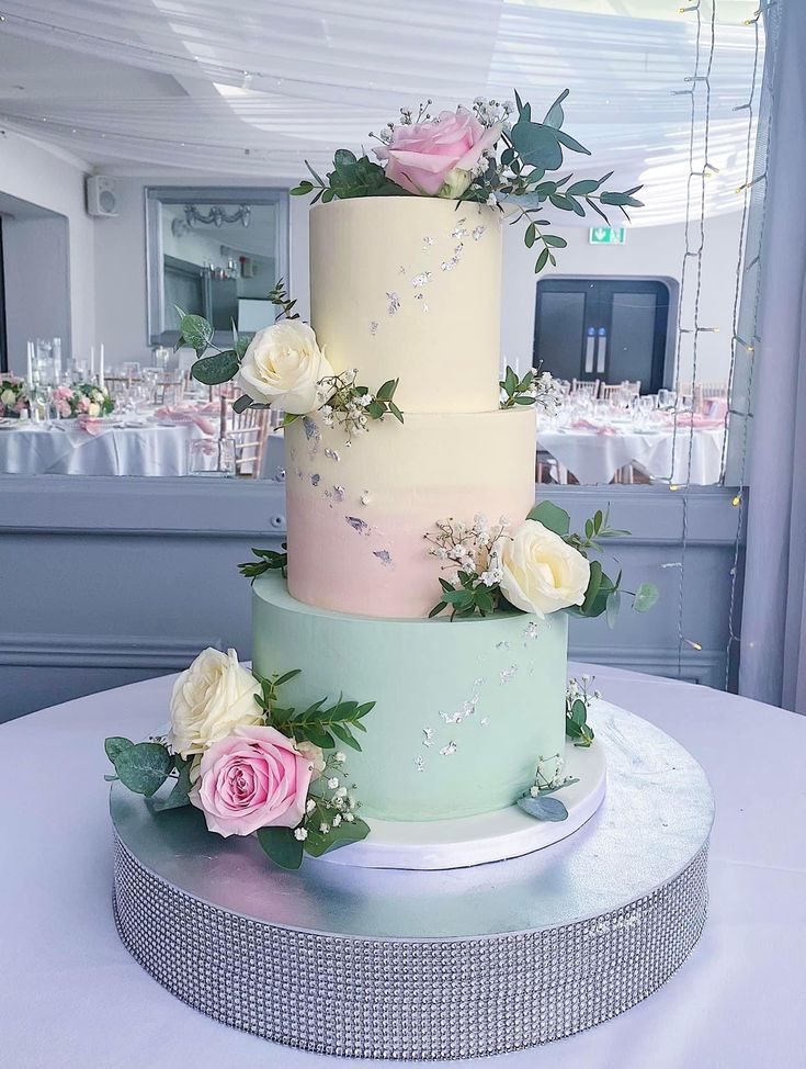 a multi - tiered cake with flowers and greenery sits on a round table