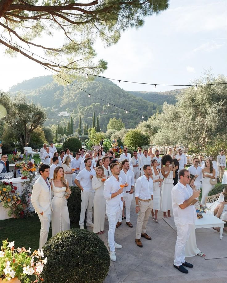 a group of people standing around each other in front of some trees and bushes on a sunny day