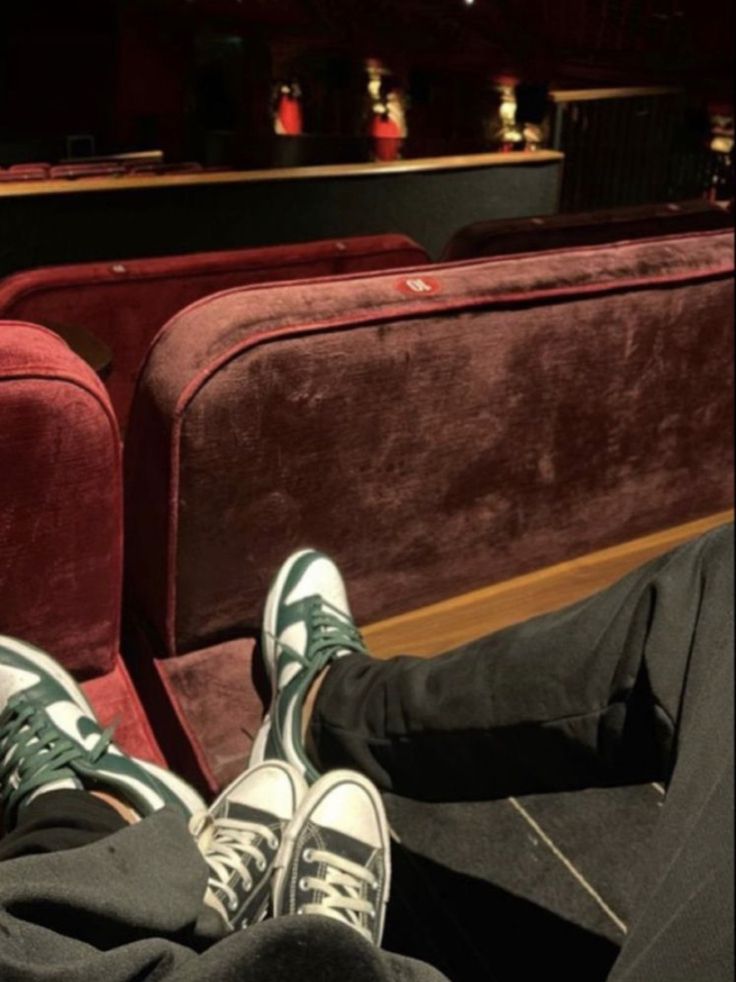 two people are sitting in an auditorium with their feet propped up on the seats and one person is wearing green sneakers