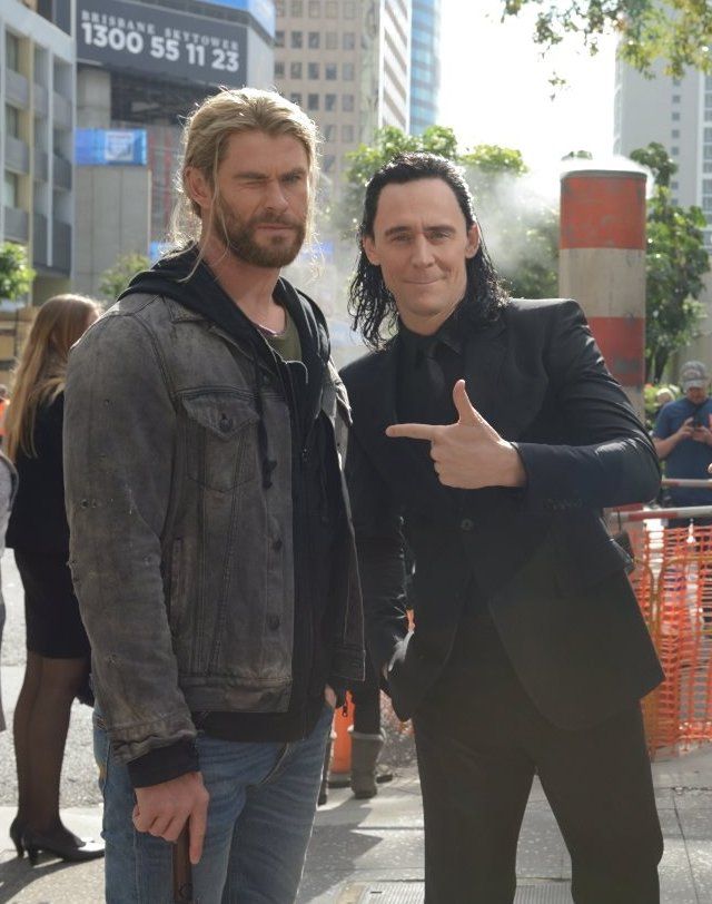 two men standing next to each other on a city street with buildings in the background