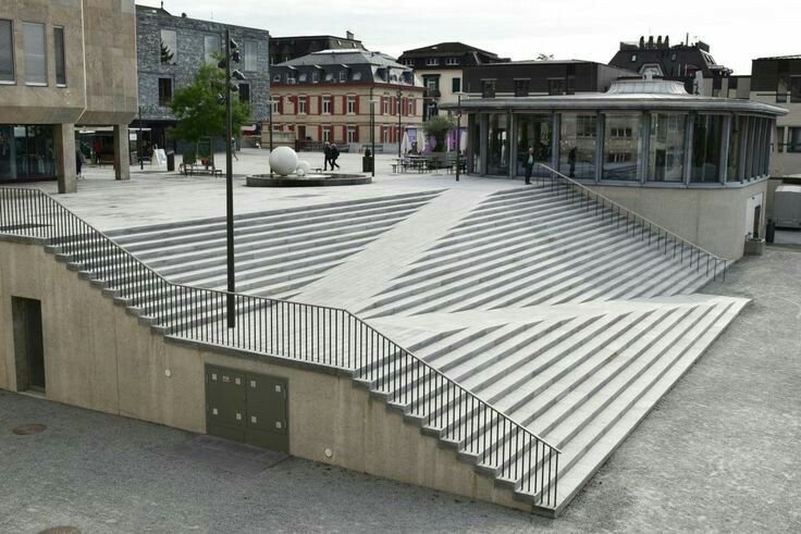 an empty parking lot with stairs leading up to the building and people walking around it