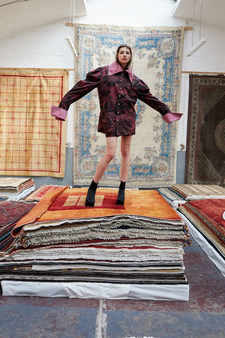 a woman standing on top of a pile of rugs