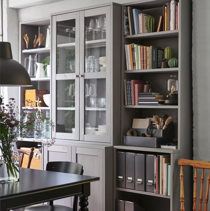 a room filled with lots of books and furniture next to a dining room table in front of a window