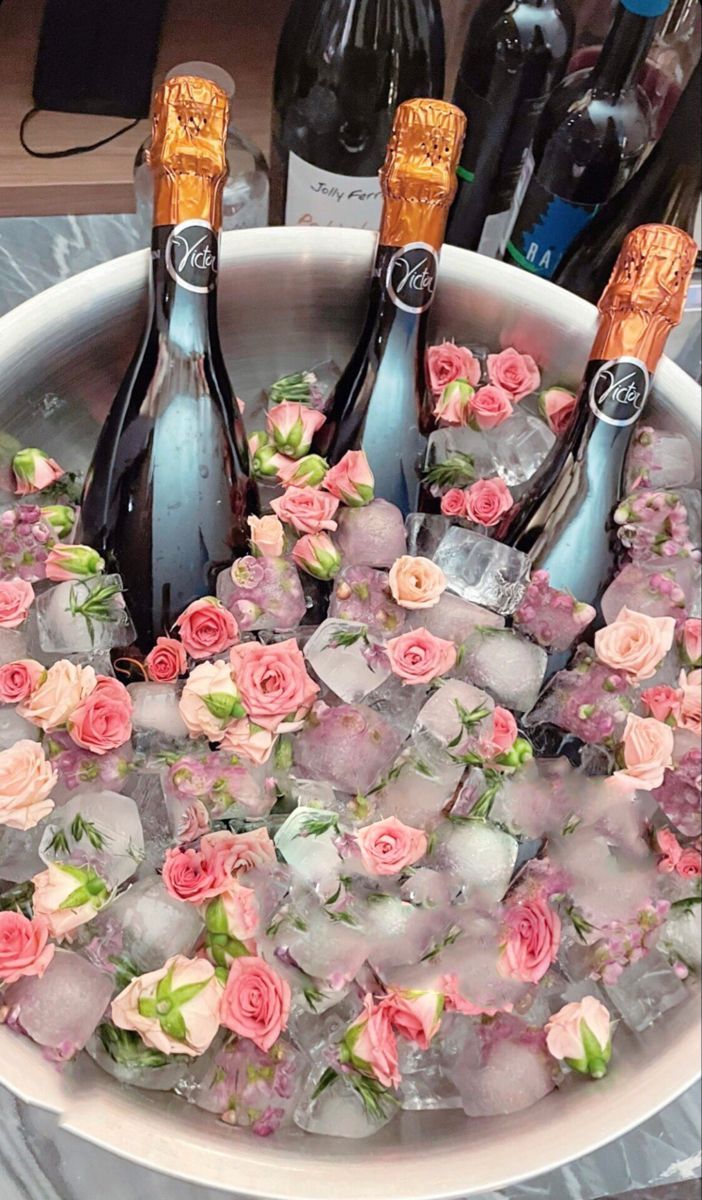 four bottles of champagne are in an ice bucket with pink flowers and roses on it