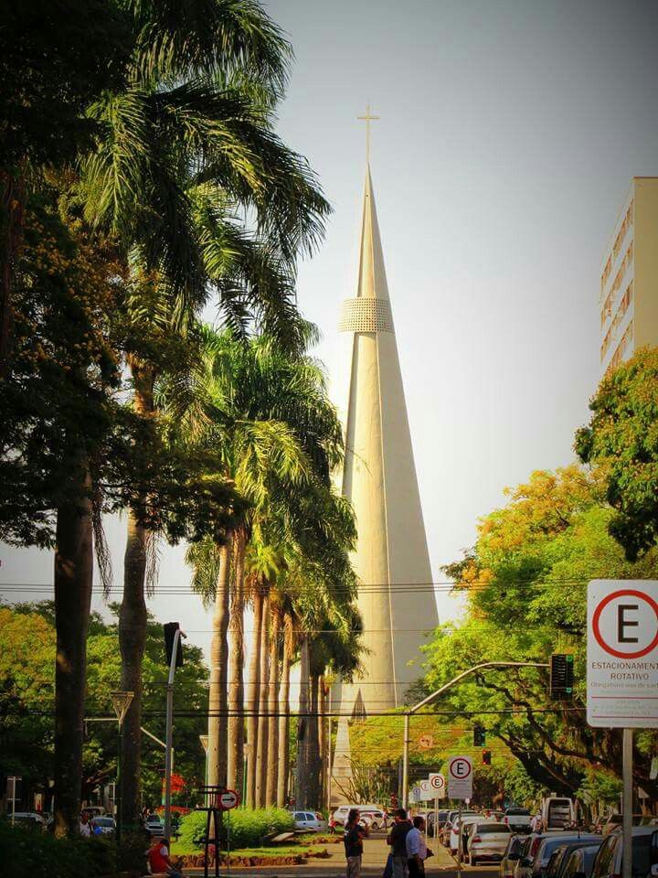 people are walking down the street in front of a tall building with a steeple