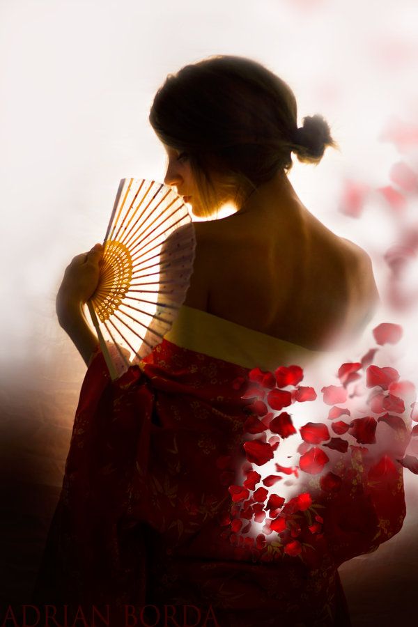 a woman in a kimono holding a fan with red flowers on the back and behind her