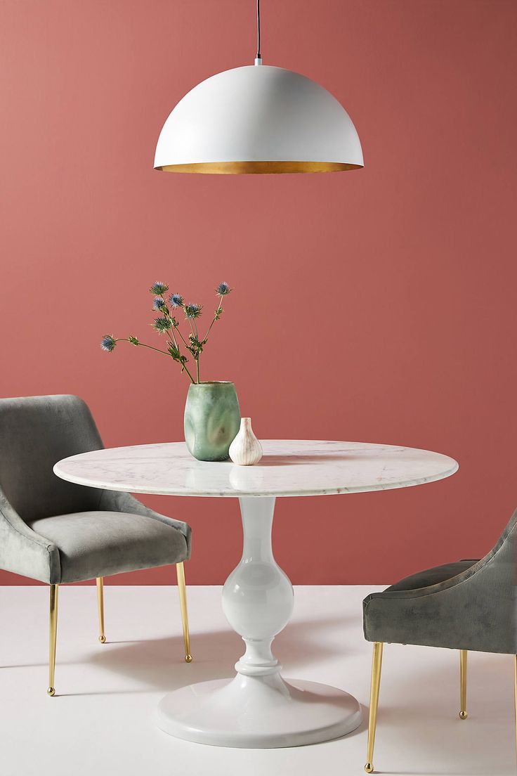 two chairs and a table in front of a pink wall with a vase on it