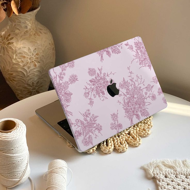 an apple laptop computer sitting on top of a white table next to yarn and spools of thread