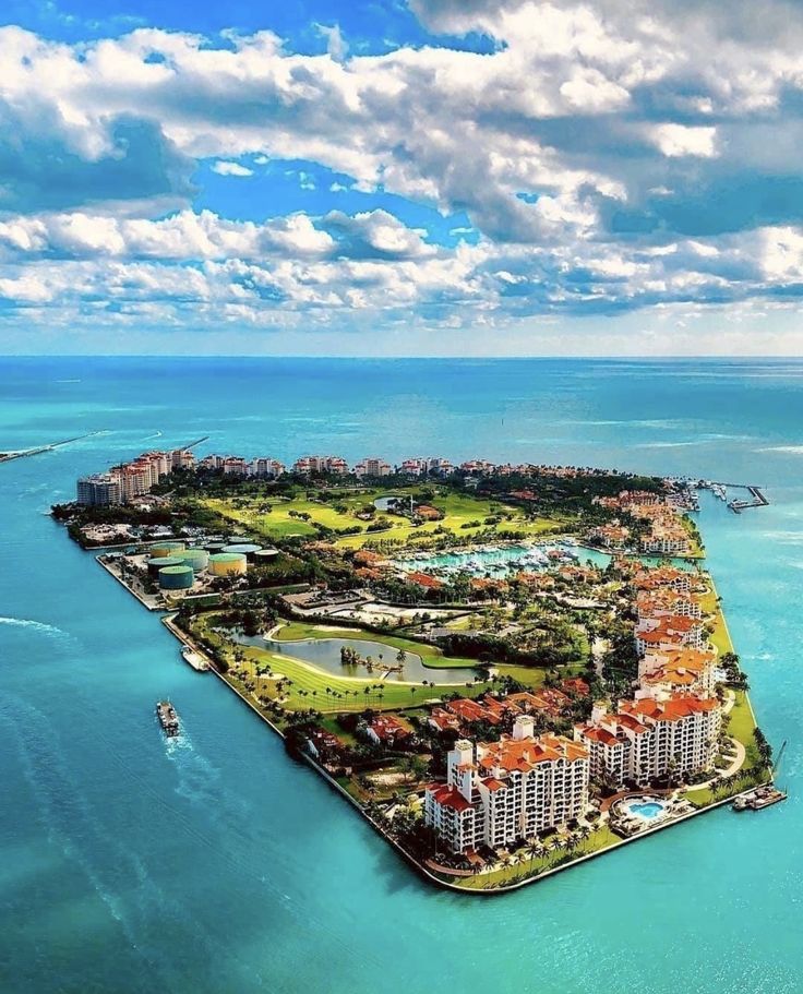 an island in the middle of the ocean with buildings on it and boats sailing by