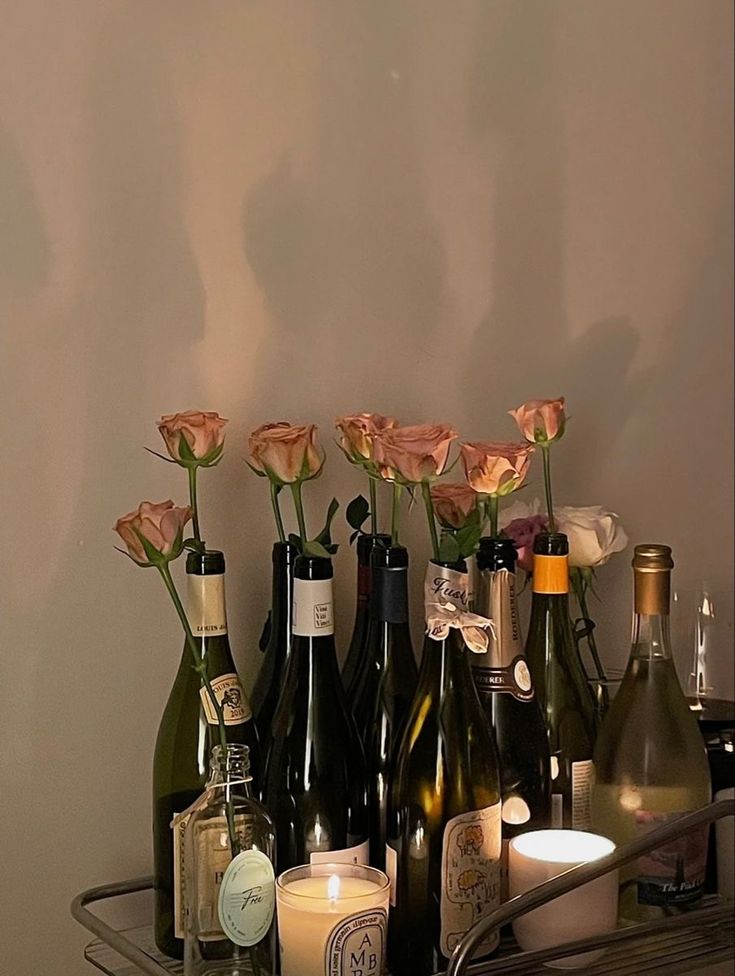 several bottles of wine and candles are arranged on a metal shelf in front of a wall