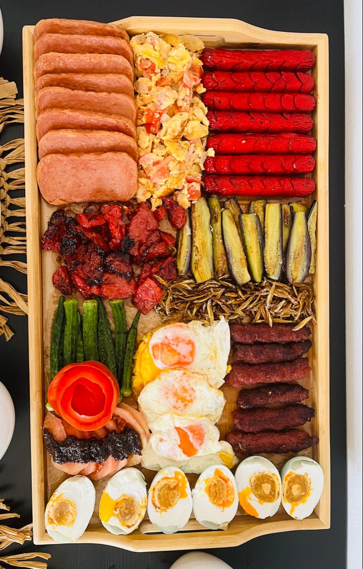 an assortment of eggs, sausages, and other foods are arranged in a wooden tray