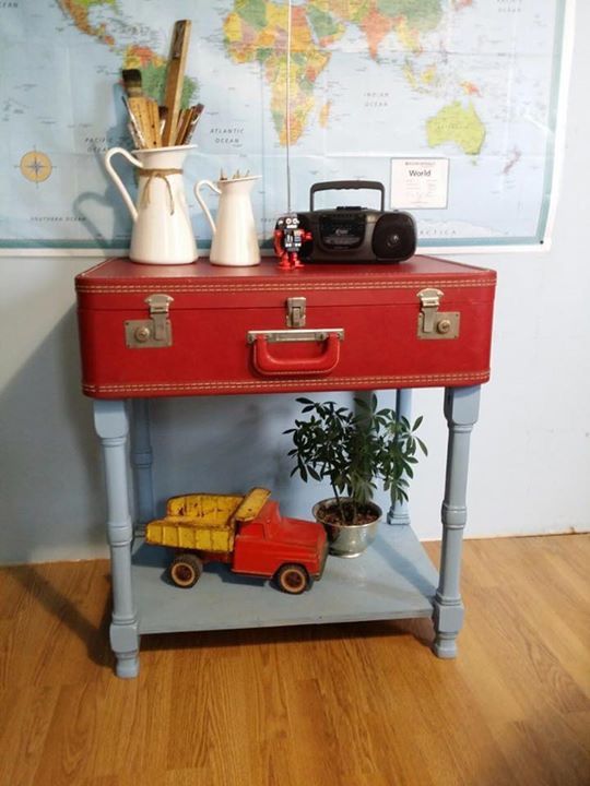 a red suitcase sitting on top of a wooden table next to a potted plant