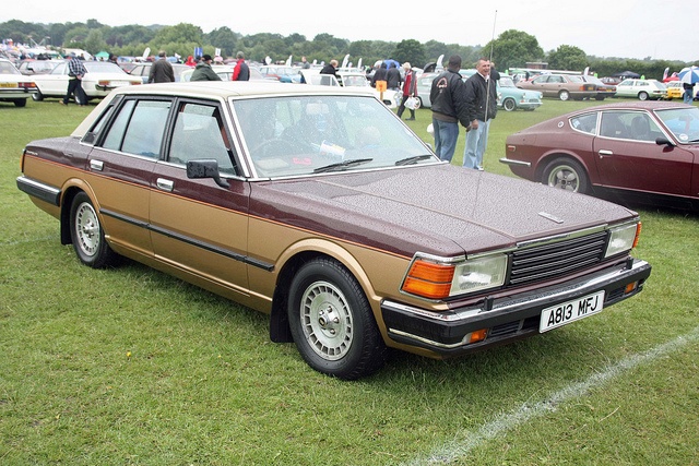 an old car parked on top of a grass covered field next to other cars in the background