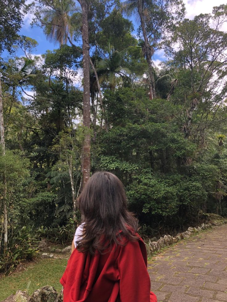 a woman in a red cape walking down a path with trees and bushes behind her