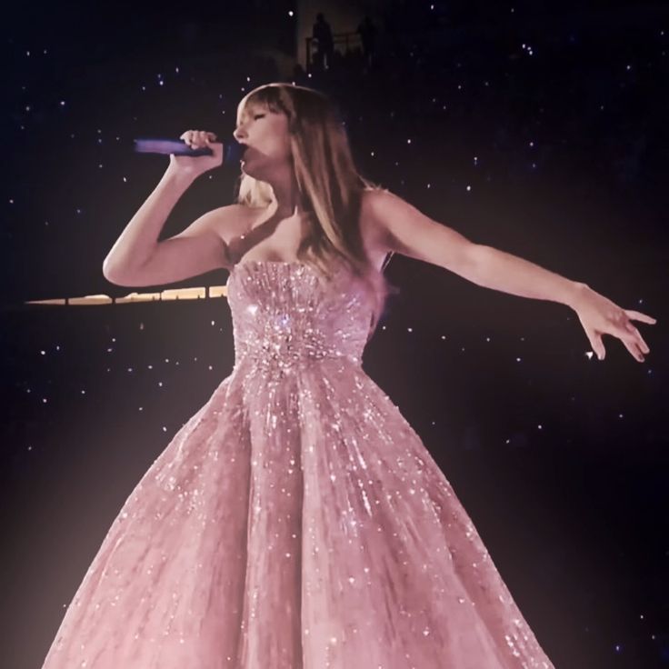 a woman in a pink dress holding a microphone and singing into the air with her arms outstretched